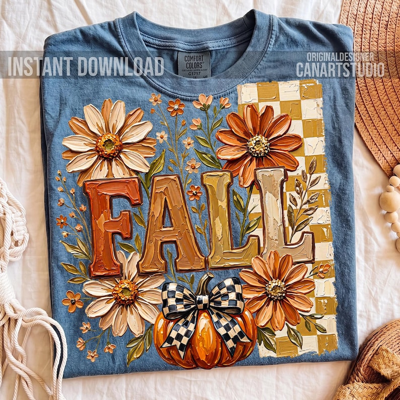 May include: Blue t-shirt with a fall-themed design. The design includes the word "FALL" in large, textured letters, surrounded by orange and cream-colored flowers, a pumpkin with a checkered bow, and the text "INSTANT DOWNLOAD" and "CANARTSTUDIO".