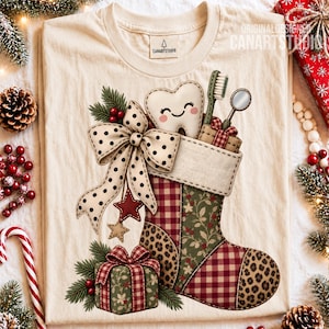 May include: A cream-colored t-shirt featuring a graphic of a Christmas stocking filled with a smiling tooth, a toothbrush, and a dental mirror. The stocking has red plaid, green floral, and leopard print patches with a large polka dot bow.