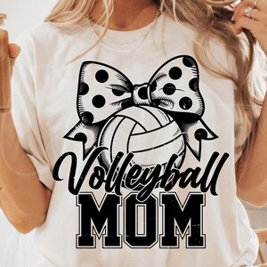 May include: White t-shirt with a black and white volleyball and bow design. The text "Volleyball Mom" is printed in black.