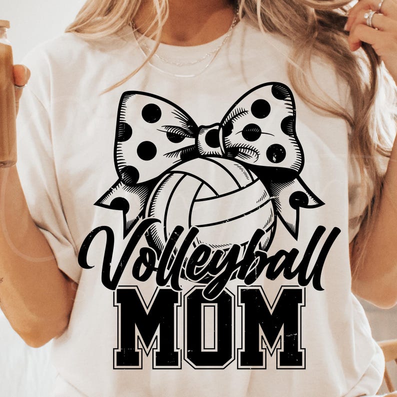 May include: White t-shirt with a black and white volleyball and bow design. The text "Volleyball Mom" is printed in black.
