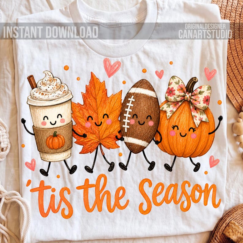 May include: A white t-shirt featuring a graphic of a coffee cup, a maple leaf, a football, and a pumpkin, all with smiling faces. The text 'tis the Season' is printed in orange below the characters, surrounded by small pink hearts and orange dots.