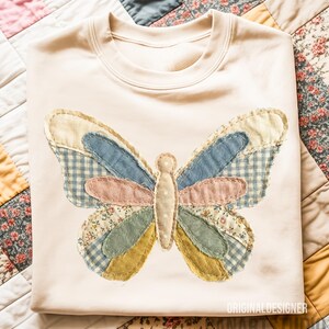 May include: Cream-colored sweatshirt featuring a large butterfly applique. The butterfly design incorporates various fabric patterns and colors, including blue gingham, floral prints, and pastel hues. The text "ORIGINALDESIGNER" and "NANARTSSTUDIO" are visible.