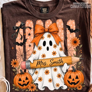 Puede incluir: Una camiseta marr&oacute;n con una ilustraci&oacute;n de un fantasma blanco con un lazo naranja, sosteniendo un l&aacute;piz amarillo grande con el texto Mrs. Smith. El dise&ntilde;o incluye flores naranjas, dos calabazas, murci&eacute;lagos negros y telara&ntilde;as sobre un fondo a rayas.