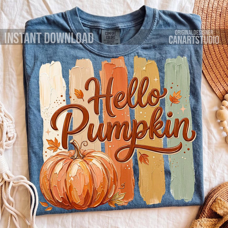 Puede incluir: Camiseta azul con un dise&ntilde;o de tem&aacute;tica oto&ntilde;al. El dise&ntilde;o presenta las palabras "Hello Pumpkin" en escritura marr&oacute;n, una calabaza naranja detallada y pinceladas verticales en varios colores. El texto "Instant Download" es visible.