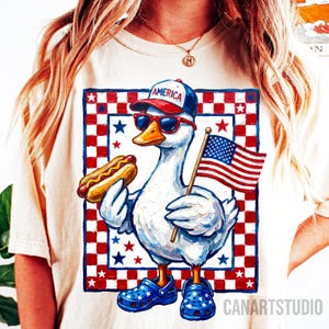 May include: Cream-colored t-shirt featuring a patriotic goose wearing sunglasses, a hat that says "AMERICA", and blue star-patterned shoes. The goose holds a hot dog and an American flag. The background has a red, white, and blue checkered pattern.