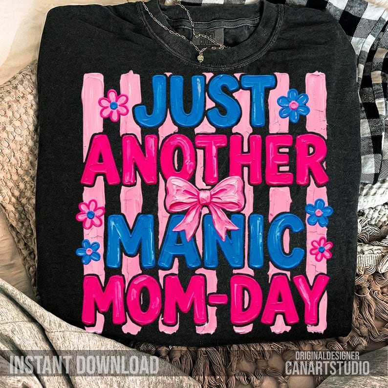Op de afbeelding: Donkergrijze sweatshirt met de tekst "JUST ANOTHER MANIC MOM-DAY" in roze en blauw, met een roze strik en bloemaccenten. De woorden zijn geplaatst tegen roze verticale strepen. De zin "INSTANT DOWNLOAD" staat onderaan.