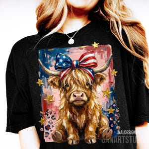 Peut inclure: T-shirt noir avec une illustration de vache des Highlands orn&eacute;e d'un n&oelig;ud patriotique et d'&eacute;toiles dor&eacute;es. La vache a de longs poils bruns et hirsutes, sur un fond de coups de pinceau rouges, blancs et bleus. Th&egrave;me patriotique.