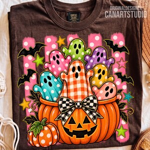 May include: A dark brown t-shirt featuring a graphic of a large orange jack-o'-lantern filled with colorful ghosts in polka dot and gingham patterns. The design includes black bats, yellow stars, and pink vertical stripes with white polka dots.
