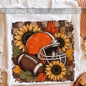 May include: A white t-shirt featuring a graphic print of an orange football helmet and a brown football surrounded by yellow sunflowers and orange autumn leaves against a brown checkered background with the text INSTANT DOWNLOAD CANARTSTUDIO.