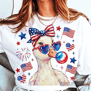 Op de afbeelding: Wit T-shirt met een eendenontwerp met een hartvormige zonnebril en een strik, met Amerikaanse vlaggen en sterren. De eend blaast een bel. Patriotisch thema.