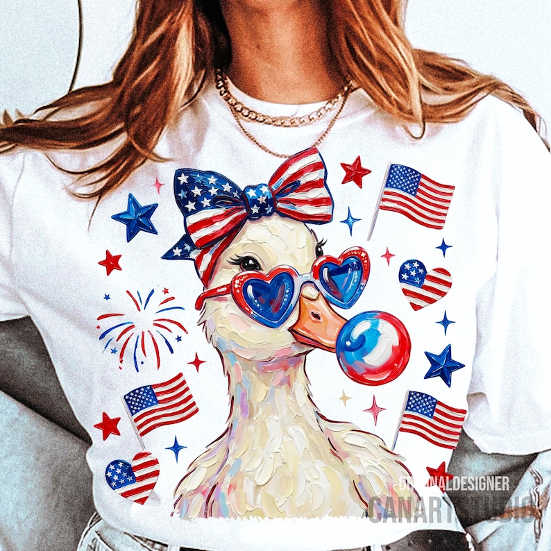 Op de afbeelding: Wit T-shirt met een eendenontwerp met een hartvormige zonnebril en een strik, met Amerikaanse vlaggen en sterren. De eend blaast een bel. Patriotisch thema.