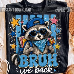 May include: A black t-shirt featuring a graphic of a raccoon wearing a blue baseball cap, heart-shaped sunglasses, and a blue bandana. The raccoon carries a blue backpack with notebooks and pencils. The text reads BRUH we back in blue letters.