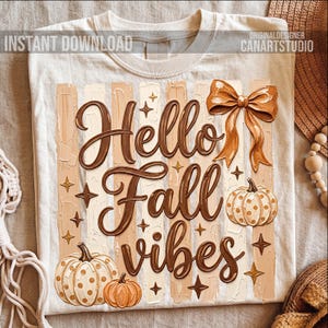 May include: A cream-coloured t-shirt with a fall design. It features the words "Hello Fall Vibes" in brown script, pumpkins, a bow, and stars. The text "Instant Download" and "Original Designer CanArtStudio" are also visible on the shirt.