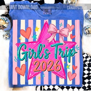 May include: Blue t-shirt with a graphic design featuring a pink star, bow, and the words "Girl's Trip 2026" in teal and orange. The design includes pink hearts and stars, with vertical pink and white stripes.