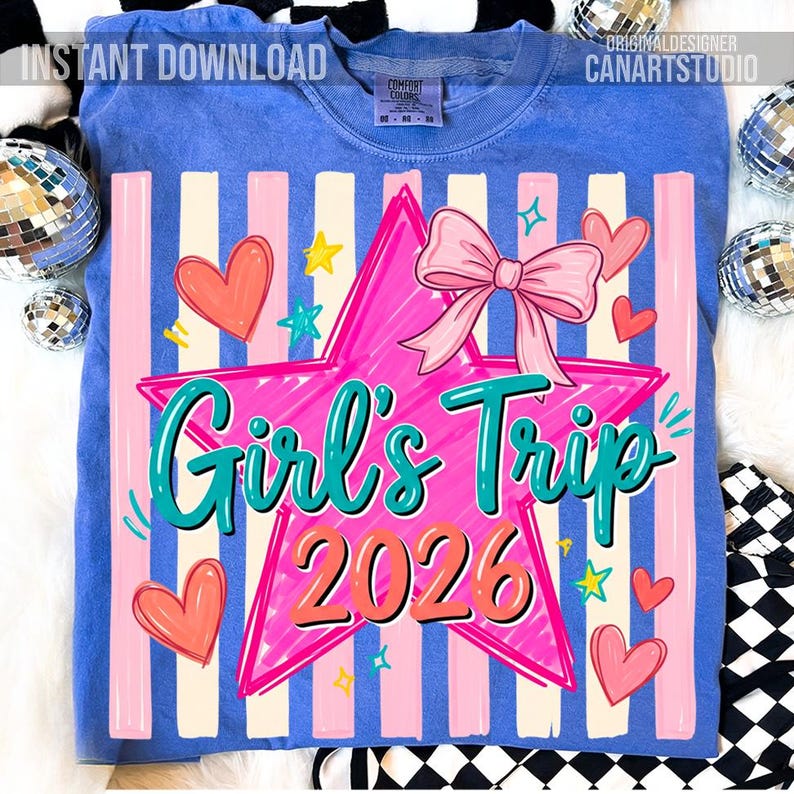 May include: Blue t-shirt with a graphic design featuring a pink star, bow, and the words "Girl's Trip 2026" in teal and orange. The design includes pink hearts and stars, with vertical pink and white stripes.
