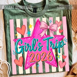 May include: Green t-shirt with a colorful graphic design. The design features a pink star with a bow, the words "Girl's Trip 2026" in teal and orange, pink and white stripes, hearts, and stars. The words "Instant Download" and "Original Designer Canartstudio" are also visible.
