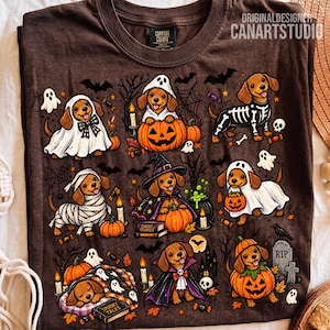 May include: A brown t-shirt featuring a graphic print of dachshunds in various Halloween costumes, including ghosts, a skeleton, a mummy, a witch, and a vampire, surrounded by pumpkins, bats, candles, and a tombstone with the text Ghost Stories.