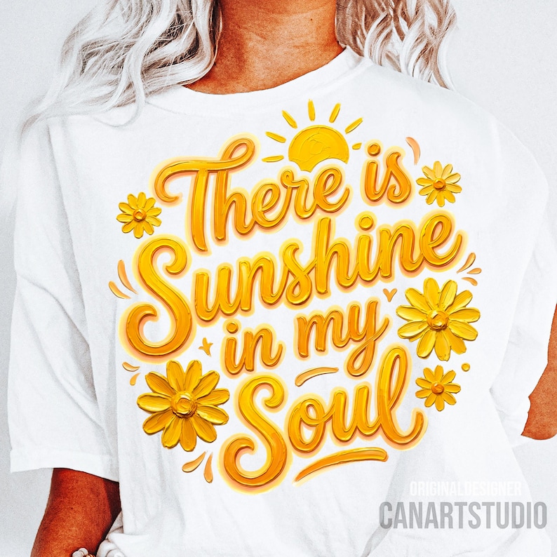 Peut inclure: T-shirt blanc avec l'inscription "There is Sunshine in my Soul" en jaune. Le motif comprend un soleil jaune et des fleurs jaunes. Les mots "Original Designer" et "CANARTSTUDIO" sont imprim&eacute;s en bas.