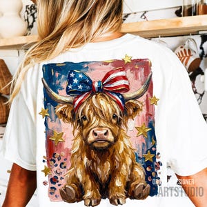 Peut inclure: T-shirt blanc avec un motif de vache des Highlands orn&eacute; d'un n&oelig;ud aux couleurs du drapeau am&eacute;ricain et d'&eacute;toiles dor&eacute;es. La vache a de longs poils bruns et hirsutes, sur un fond de coups de pinceau rouges, blancs et bleus. Le t-shirt porte le texte "ORIGINAL DESIGNER ARTSTUDIO".