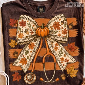 May include: A dark brown t-shirt featuring a graphic of a large cream-colored bow with lace edges, decorated with orange pumpkins, acorns, and autumn leaves. An orange stethoscope is integrated into the design. Text reads ORIGINALDESIGNER CANARTSTUDIO.