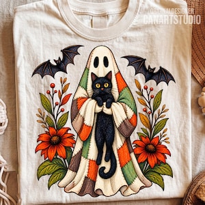 Può includere: Una t-shirt color crema con la grafica di un gatto nero che indossa un costume da fantasma patchwork. Il disegno include due pipistrelli in volo, fiori arancioni e fogliame verde. Il testo ORIGINALDESIGNER CANARTSTUDIO è stampato in alto a destra.