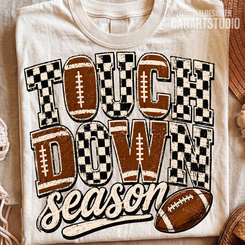 May include: A cream-colored t-shirt featuring the text TOUCH DOWN SEASON in a mix of brown football-textured letters and black-and-white checkered patterns. A brown football graphic is positioned at the bottom right of the design.