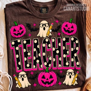 May include: A brown t-shirt featuring a graphic print with the word TEACHER in large black letters with white polka dots and a pink outline. The design includes three pink jack-o'-lanterns, three white ghosts wearing glasses, and yellow pencils.