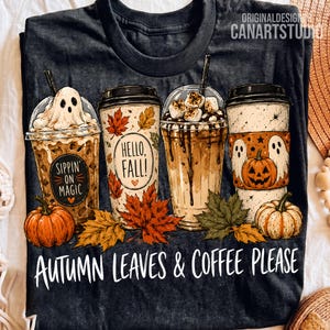 May include: A black t-shirt featuring a graphic of four coffee cups decorated with autumn themes, including ghosts, pumpkins, and maple leaves. The text reads Sippin' on Magic, Hello, Fall!, and Autumn Leaves & Coffee Please in white lettering.