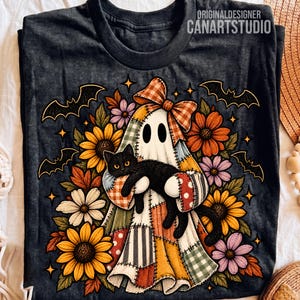 Può includere: Una t-shirt grigio scuro con la grafica di un fantasma patchwork che indossa un fiocco a quadri e tiene in braccio un gatto nero. Il fantasma è circondato da girasoli colorati, foglie autunnali e pipistrelli neri. Il testo ORIGINALDESIGNER CANARTSTUDIO è visibile.