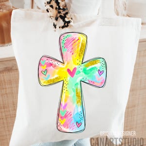 Op de afbeelding: Een witte draagtas met een kleurrijk kruisontwerp. Het kruis is beschilderd met aquarel-achtige penseelstreken in roze, geel, groen en blauw, met gouden glitteraccenten en hartdetails. De tekst "CANARTSTUDIO" is zichtbaar.