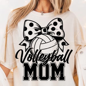 May include: White t-shirt with a black and white graphic of a volleyball with a polka dot bow and the text "Volleyball Mom".