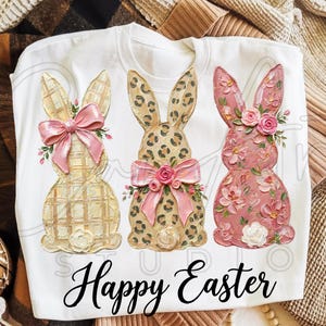Puede incluir: Sudadera blanca de cuello redondo con tres dise&ntilde;os de conejitos de Pascua. Los conejitos tienen patrones texturizados, lazos y detalles florales. El texto "Happy Easter" est&aacute; impreso en una fuente cursiva en la parte inferior.
