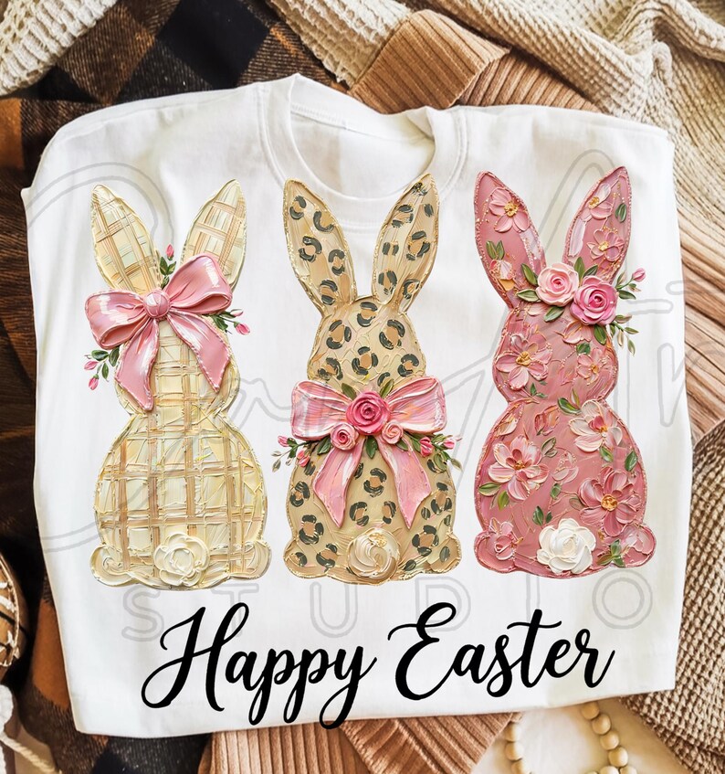 Puede incluir: Sudadera blanca de cuello redondo con tres dise&ntilde;os de conejitos de Pascua. Los conejitos tienen patrones texturizados, lazos y detalles florales. El texto "Happy Easter" est&aacute; impreso en una fuente cursiva en la parte inferior.