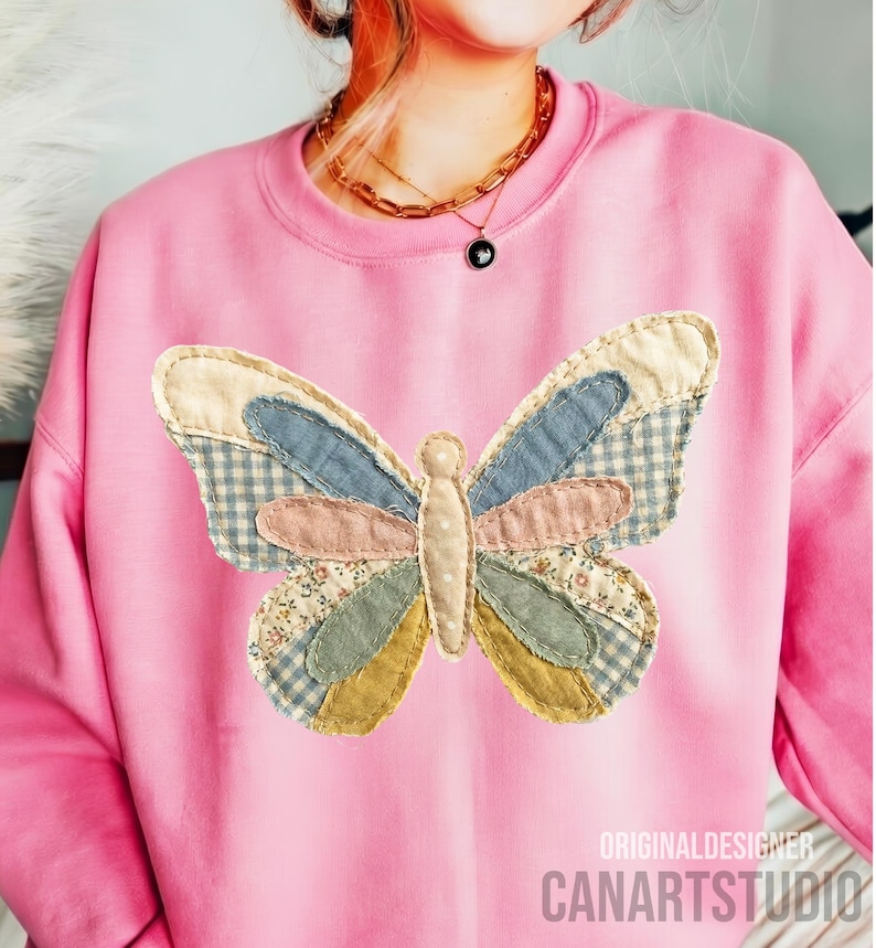 May include: Pink sweatshirt featuring a patchwork butterfly design. The butterfly has wings in various colors and patterns, including blue gingham, floral, and solid fabrics. The text "ORIGINALDESIGNER CANARTSTUDIO" is printed on the bottom right.