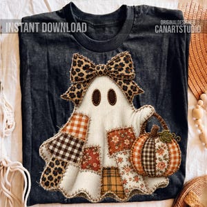 Pode incluir: Uma t-shirt cinzento-escura com um gráfico central de um fantasma branco adornado com um laço de padrão leopardo. O fantasma é composto por vários retalhos de tecido com padrões xadrez, florais e animais, e segura uma pequena abóbora.