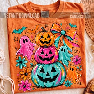 Op de afbeelding: Oranje T-shirt met een Halloween-thema ontwerp. Het ontwerp toont gestapelde pompoenen met uitgesneden gezichten, geesten, vleermuizen en bloemen. De tekst "INSTANT DOWNLOAD" en "CANARTSTUDIO" zijn zichtbaar. Gemaakt door Comfort Colors.