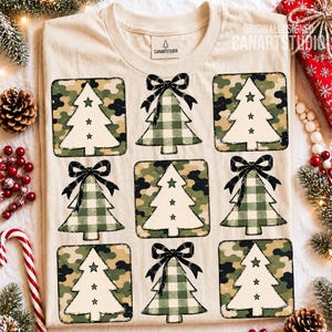 Könnte beinhalten: Ein beiges T-Shirt mit einem Raster aus neun Weihnachtsmotiv-Grafiken. Die Bäume wechseln zwischen weißen Silhouetten auf Camouflage-Hintergrund und grünen Vichy-Karomustern mit schwarzen Schleifen. Jeder Baum hat drei kleine Stern-Ausstanzungen.