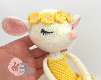Puede incluir: Un cordero blanco de crochet que lleva una corona de flores amarillas y un vestido amarillo con una falda de tul blanca. El cordero tiene orejas rosas y una nariz rosa.