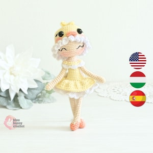 May include: A handmade crochet doll in a yellow dress with white trim and a matching hat. The doll has a smiling face, white hair, and peach-coloured accents. The doll is approximately 15 cm tall.