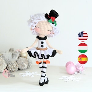 Pode incluir: Boneca de crochê feita à mão com um vestido branco, detalhes em preto e um pequeno chapéu alto preto adornado com bagas vermelhas e folhas verdes. A boneca tem cabelo branco encaracolado e meias listradas. A boneca tem cerca de 20 cm de altura.