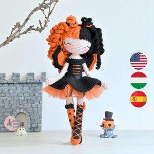 Puede incluir: Muñeca de ganchillo hecha a mano con pelo naranja y negro, un vestido negro y una falda de tul naranja. La muñeca tiene botas naranjas y negras y está de pie frente a un castillo en miniatura y una pequeña figura de calabaza. Tema de Halloween.