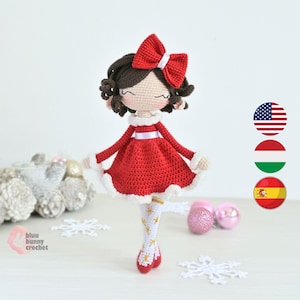 Pode incluir: Boneca de crochê feita à mão, vestindo um vestido vermelho com acabamento branco e um laço vermelho a condizer. A boneca tem cabelo castanho e usa meias brancas e douradas. A boneca tem cerca de 20 cm de altura.