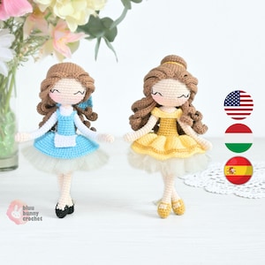May include: Two handmade crochet dolls, one in a blue dress with a white apron and the other in a yellow dress. Both dolls have brown curly hair and are standing on a white surface. The dolls are approximately 15 cm tall.