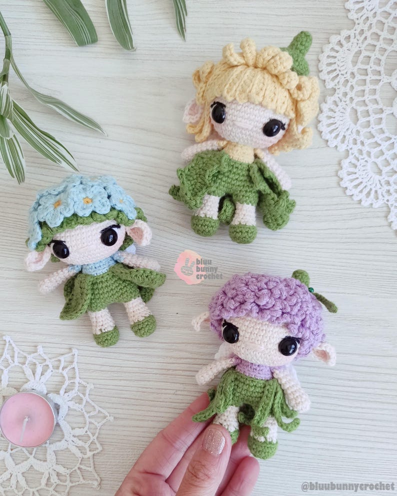 Puede incluir: Tres mu&ntilde;ecas de ganchillo hechas a mano con pelo en forma de flor y faldas verdes. Una mu&ntilde;eca tiene el pelo azul claro con detalles de flores azules, otra tiene el pelo rubio y la tercera tiene el pelo morado. Las mu&ntilde;ecas tienen ojos negros grandes.
