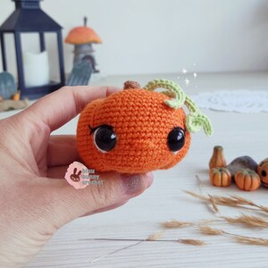 May include: A crocheted pumpkin with a green stem and black eyes. The pumpkin is orange and has a cute, cartoon-like expression.