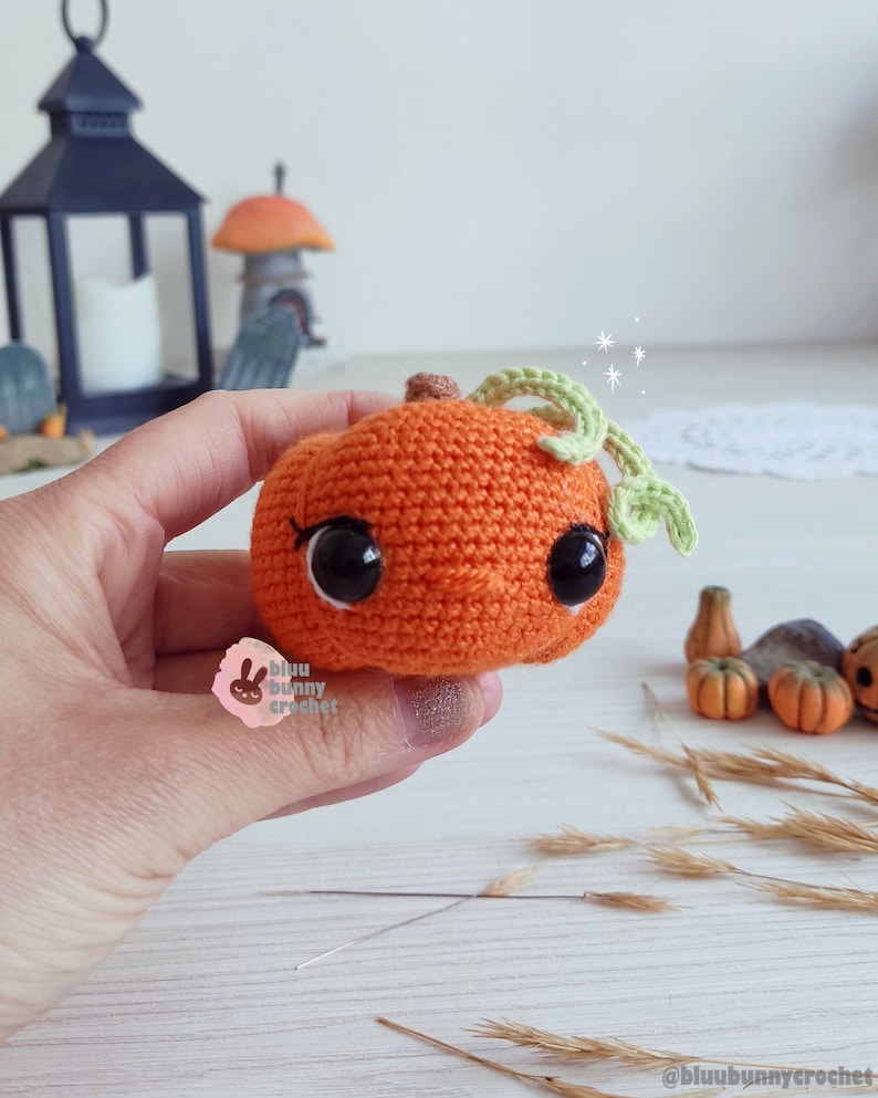 May include: A crocheted pumpkin with a green stem and black eyes. The pumpkin is orange and has a cute, cartoon-like expression.