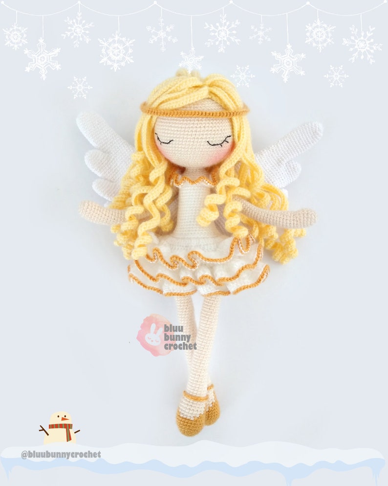 May include: A crocheted angel doll with blonde hair, white wings, and a white dress with gold trim. The doll is standing on a snowy surface with snowflakes in the background. The text "bluu bunny crochet" is visible in the image.