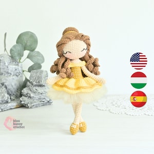 Könnte beinhalten: Handgemachte Häkelpuppe in einem gelben Kleid mit Tüllrock. Die Puppe hat braune Locken und geschlossene Augen. Die Puppe steht auf einer weißen Oberfläche. Die Puppe ist eine Prinzessinnenpuppe.