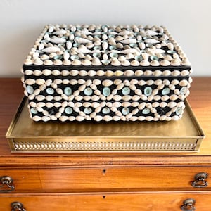 May include: A black wooden box decorated with a mosaic of white and blue seashells. The box is sitting on a brass tray.