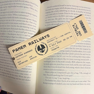 Może przedstawiać: Żółty i brązowy bilet kolejowy z nadrukiem "Panem Railways". Bilet ma jako cel "The Capitol" i datę "4 lipca 2312". Bilet ma również numer wagonu "012" i nazwisko pasażera "Katniss Everdeen".